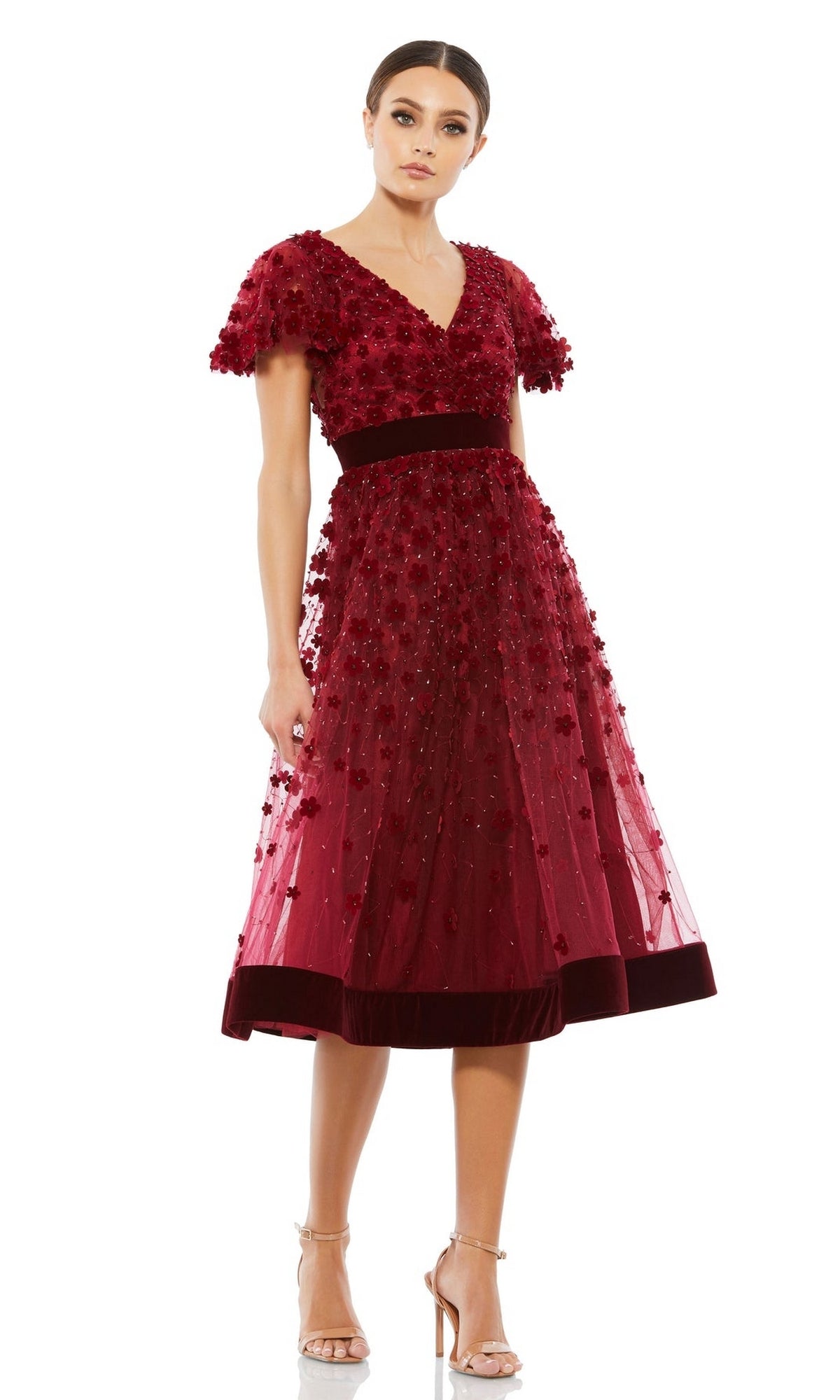 A woman in the Mac Duggal 67854 Floral Midi Wedding Guest Dress with short sleeves and velvet waistband pairs it with nude heels, creating a charming vintage-inspired look.